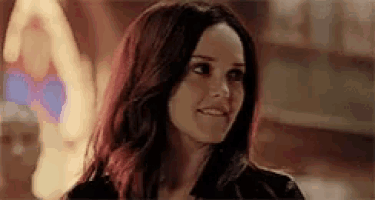 a woman with red hair is smiling and looking at the camera in a dark room .