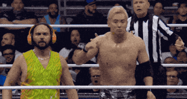 a wrestler wearing headphones stands in a ring with a referee and another wrestler