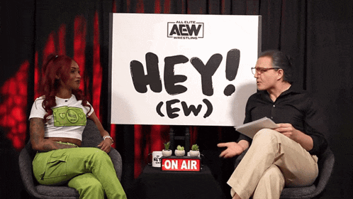a man and woman sit in front of a sign that says hey