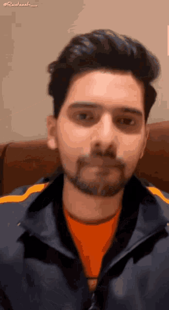 a man with a beard wearing a blue jacket and an orange shirt