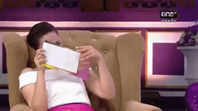 a woman is sitting in a chair holding a piece of paper in front of her face with the number one on the bottom right