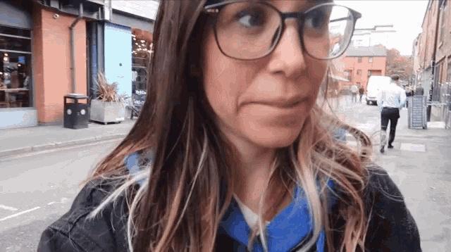 a woman wearing glasses and a blue shirt looks at the camera
