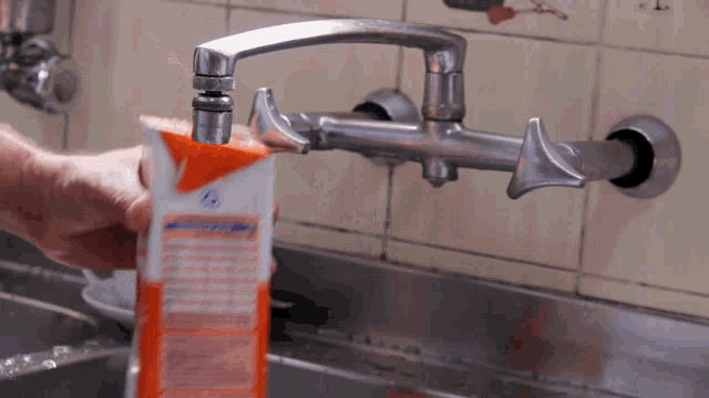 a carton of orange juice is being poured from a faucet
