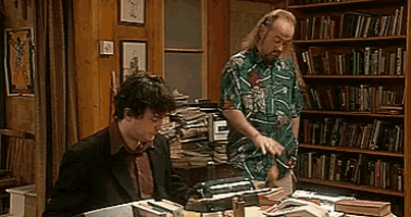 a man in a green shirt is standing next to a man in a suit in a library