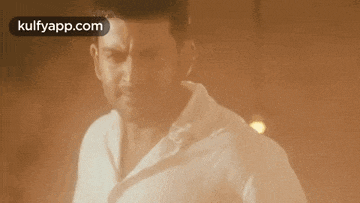 a man in a white shirt is standing in a dark room with the words kulfyapp.com in the corner