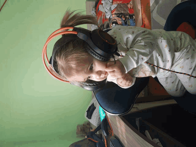 a baby wearing headphones with a ponytail looks at the camera