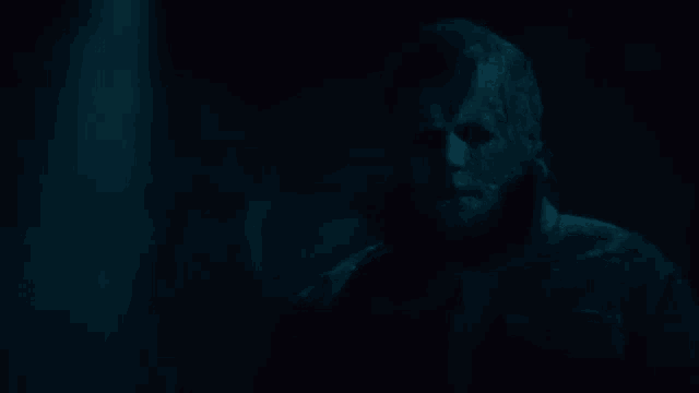 a man with a mask on his face is standing in the dark looking at the camera .