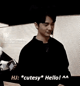 a man in a black shirt is standing in front of a wall with his mouth open and says hello .