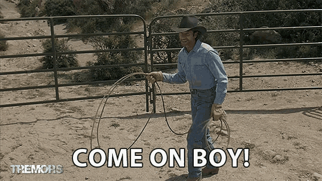 a man in a cowboy hat is holding a lasso in front of a fence that says come on boy