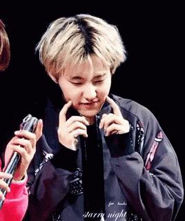 a young man with blonde hair is holding a microphone in his hand and covering his face with his hands .