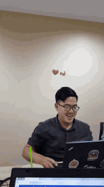 a man sitting at a desk with a laptop and a heart on the wall above him
