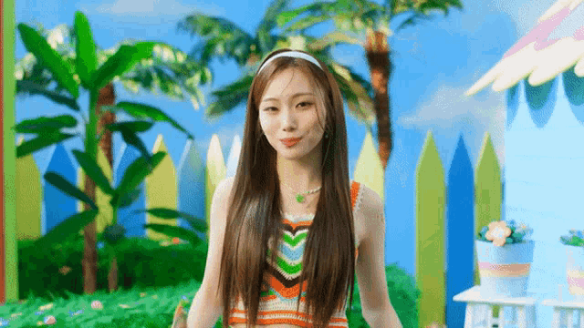 a young woman with long hair is standing in front of a fence and palm trees .