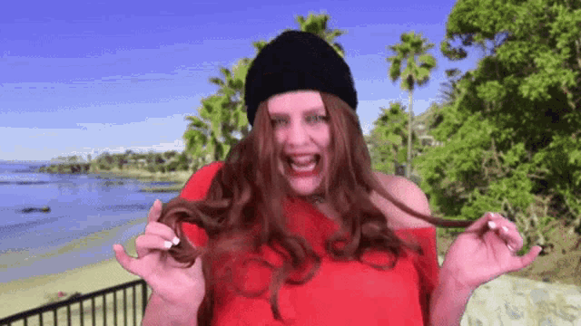 a woman wearing a black hat and a red top is holding her hair