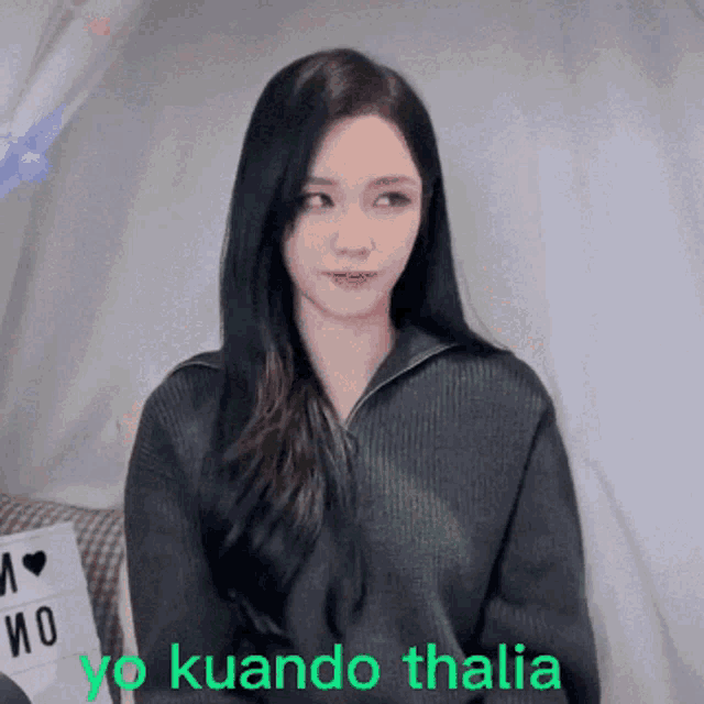 a woman with long black hair is wearing a black sweater with the words yo kuando thalia in green letters