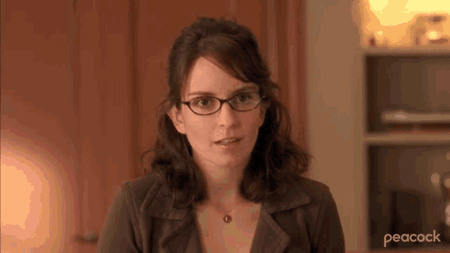 a woman wearing glasses and a peacock logo is looking at the camera