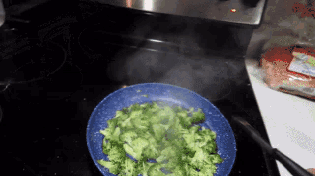 broccoli is being cooked in a blue pan on a stove top
