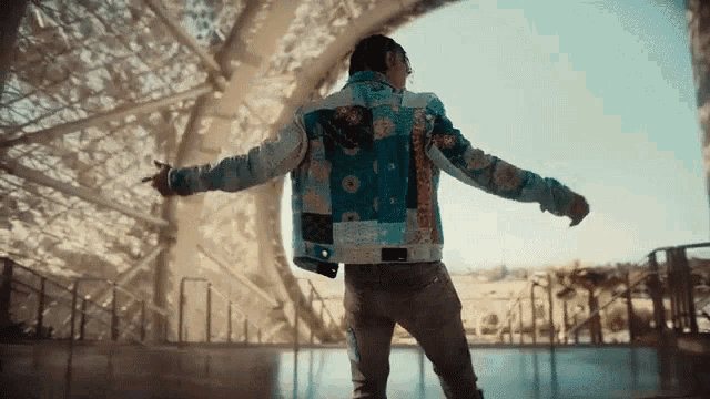 a man in a colorful jacket is standing with his arms outstretched in front of a building