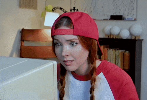 a woman wearing a red hat looks at a computer monitor