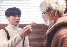 two young men are standing next to each other in a room . one of the men is wearing a face mask .