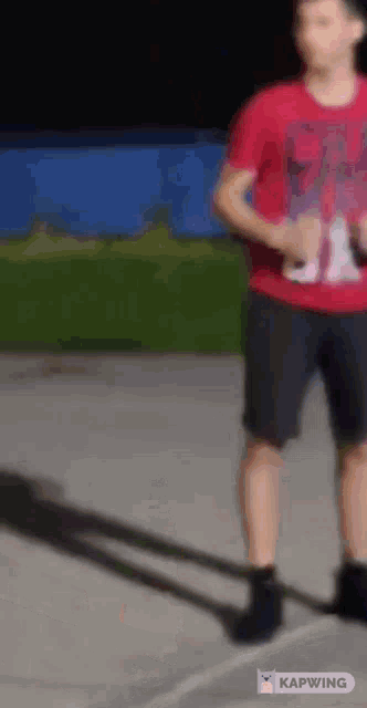 a man in a red shirt and black shorts is standing on a concrete surface .