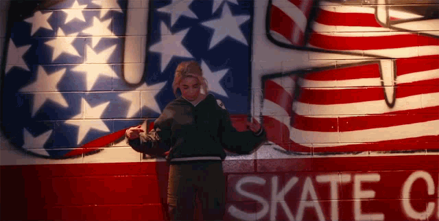 a girl stands in front of a wall that says skate on it