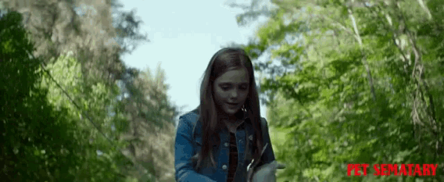 a girl in a denim jacket is holding a knife with the words pet sematary written on the bottom