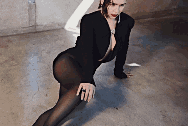 a woman in a black bodysuit and tights is kneeling on the floor