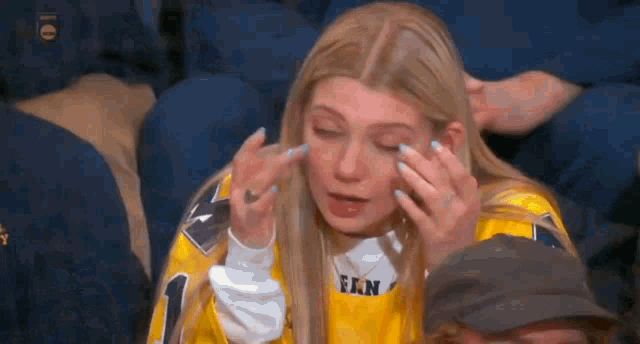 a woman in a yellow jersey is crying in a crowd .