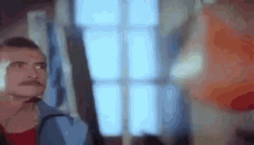 a man with a mustache is looking at himself in a mirror in a room .