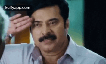 a man with a mustache is holding his hand to his forehead and making a funny face .