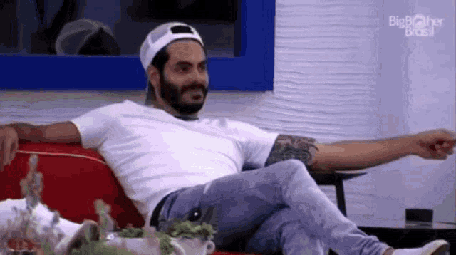 a man with a beard is sitting on a red couch and pointing .