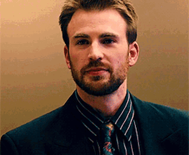 a man with a beard is wearing a black suit and tie