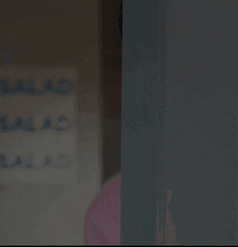 a young man in a pink sweater is peeking out from behind a wall .