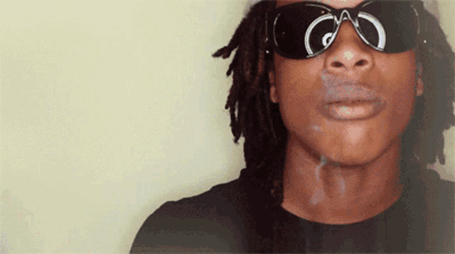 a man with dreadlocks wearing sunglasses is smoking a cigarette