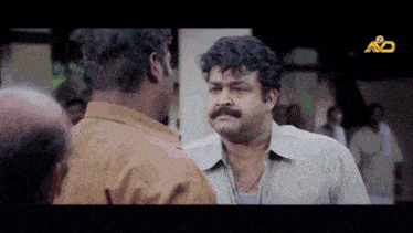 a man with a mustache is talking to another man with a yellow a on the bottom of the screen