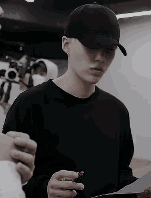 a man wearing a black hat and a black sweater is holding a piece of paper and a lighter .