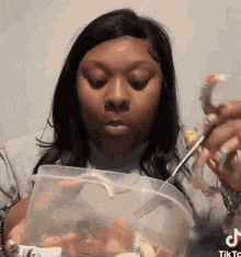 a woman is eating a bucket of food with a fork and spoon .