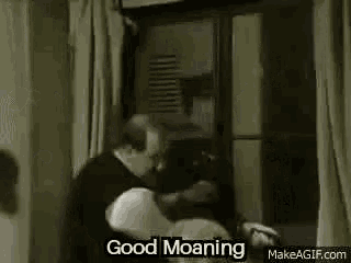 a man is standing in front of a window with a woman laying on a bed and saying `` good moaning '' .
