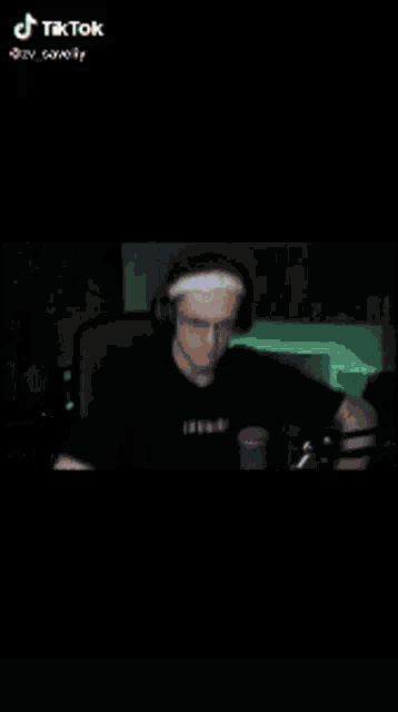 a man is sitting at a table in a dark room with his hands in his pockets .