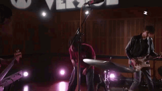 a man is singing into a microphone while another man plays a guitar and drums .