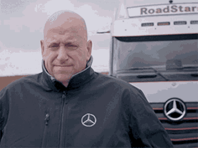 a bald man stands in front of a mercedes truck