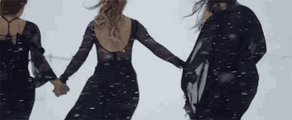 three women in long black dresses are holding hands in the snow .