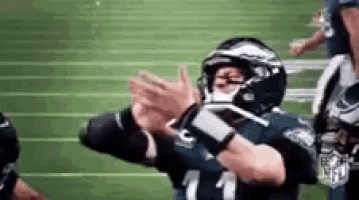 a football player is clapping his hands on a field while wearing a helmet .