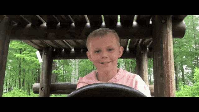 a young boy in a pink shirt is sitting in a wooden structure .