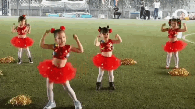 a group of young girls in red tutus are dancing on a soccer field .