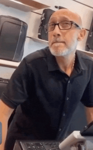 a bald man wearing glasses and a black shirt is standing in front of a counter in a store .