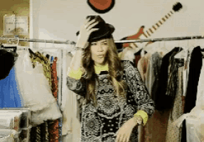 a woman wearing a hat is standing in front of a rack of clothes