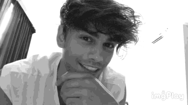 a black and white photo of a young man with his hand on his chin .