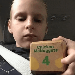 a young boy is holding a box of chicken mcnuggets number 4