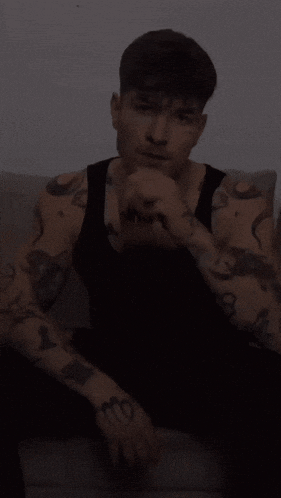 a man with a lot of tattoos on his arms is sitting on a couch .